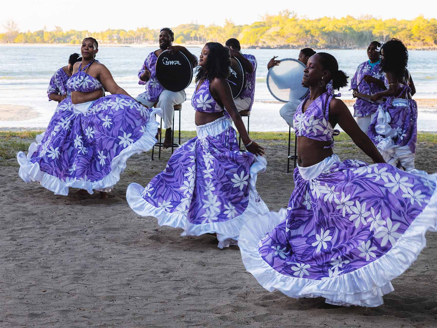Cérémonie du Tir Traka avec trois danseuses au premier plan et musiciens en arrière plan