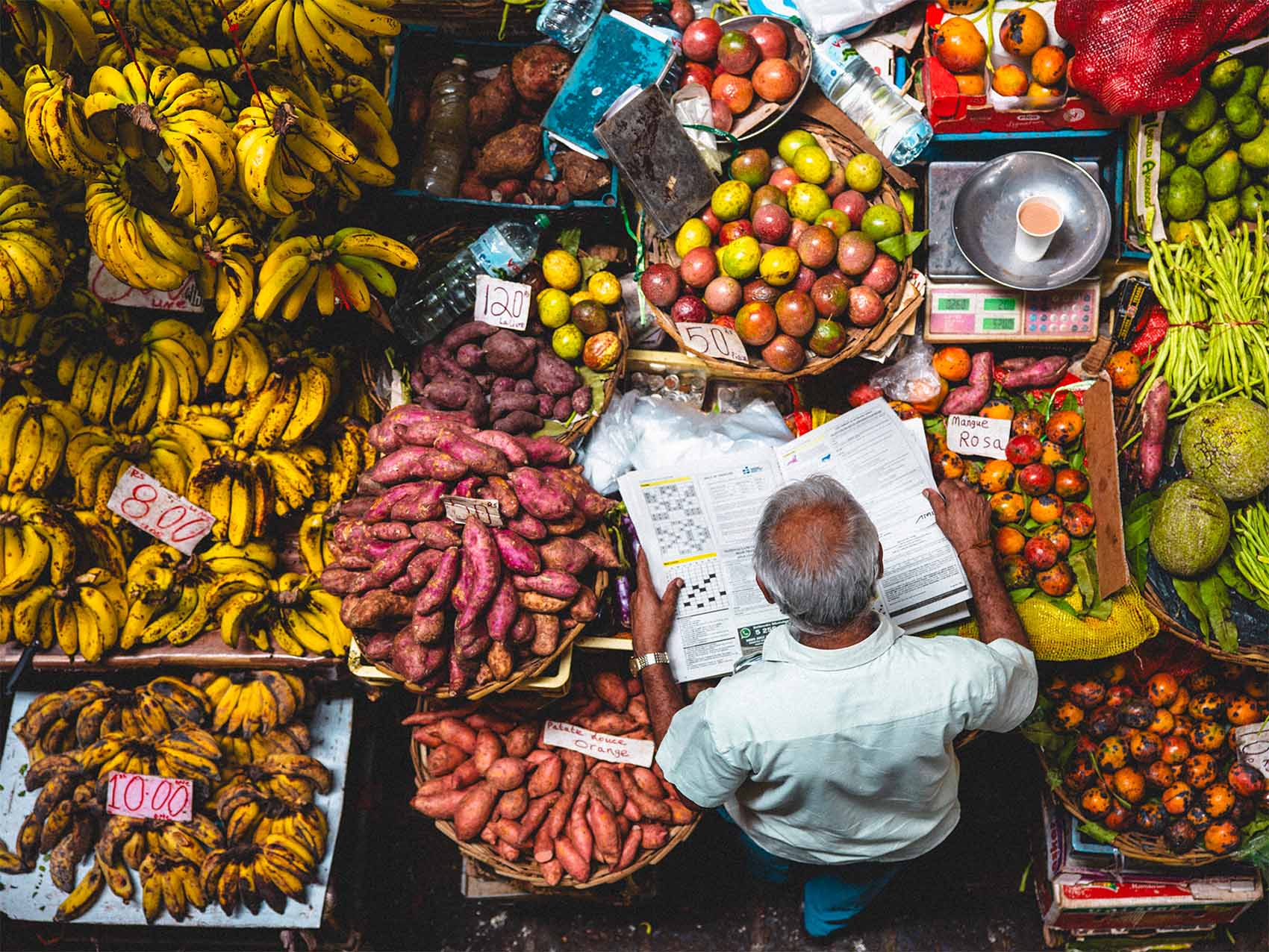 Homme qui lit son journal au marché de Port Louis à l'Île Maurice. Il est entouré de fruits